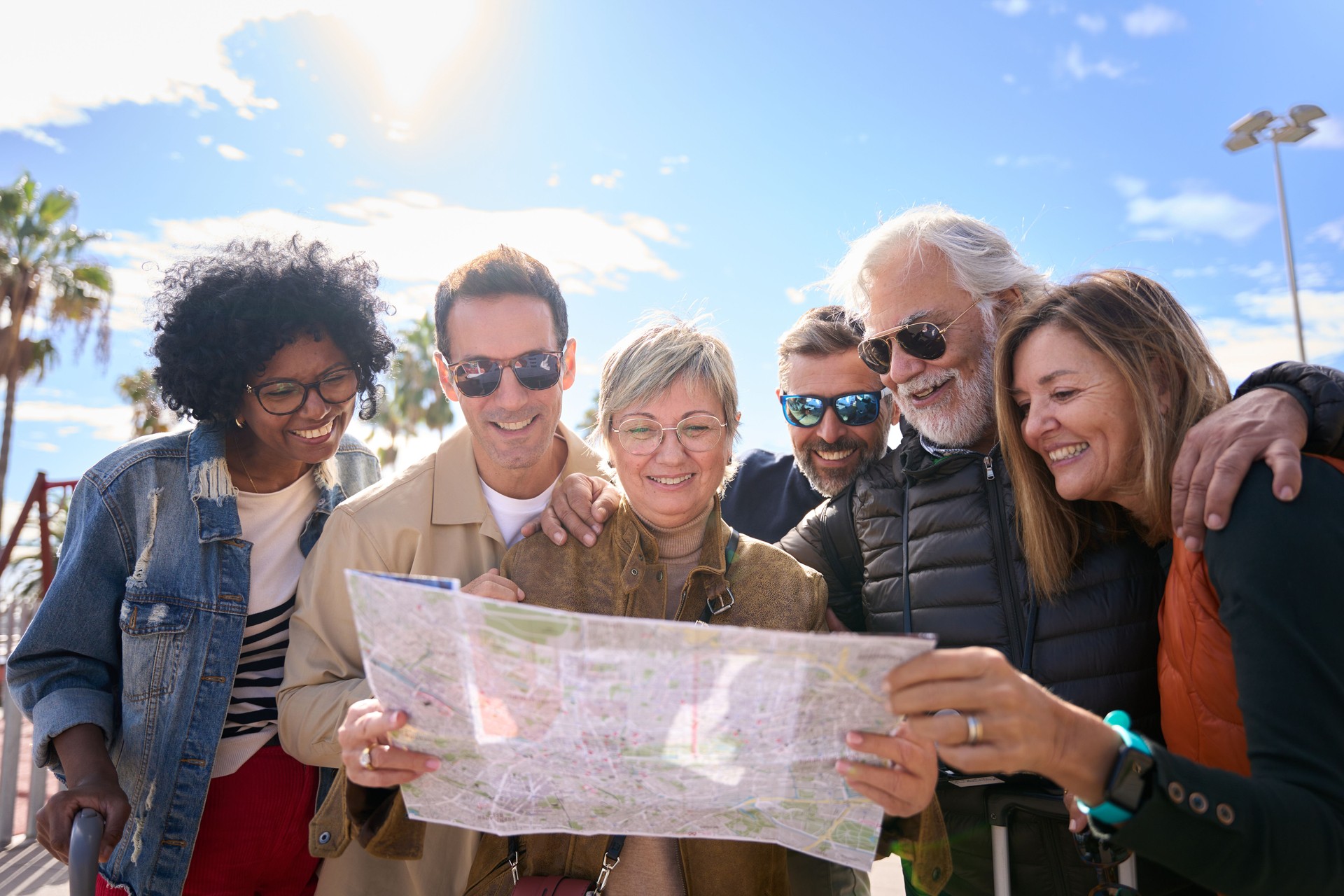 Group diverse middle-aged tourist people standing looking at travel map in hands on vacation city.